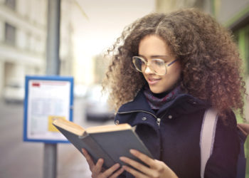 Student reading book by bus stop